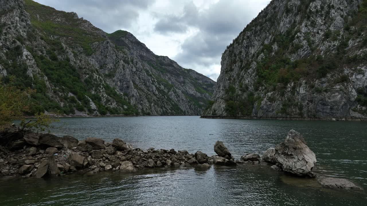 Rocky canyon frames the winding waters of Lake Koman, Albania, low establishing natural dolly of rugged mountainous terrain