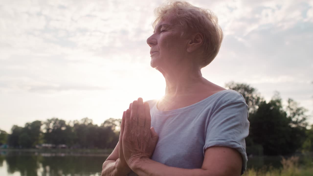 mujer mayor tranquila meditando en el parque junto al lago