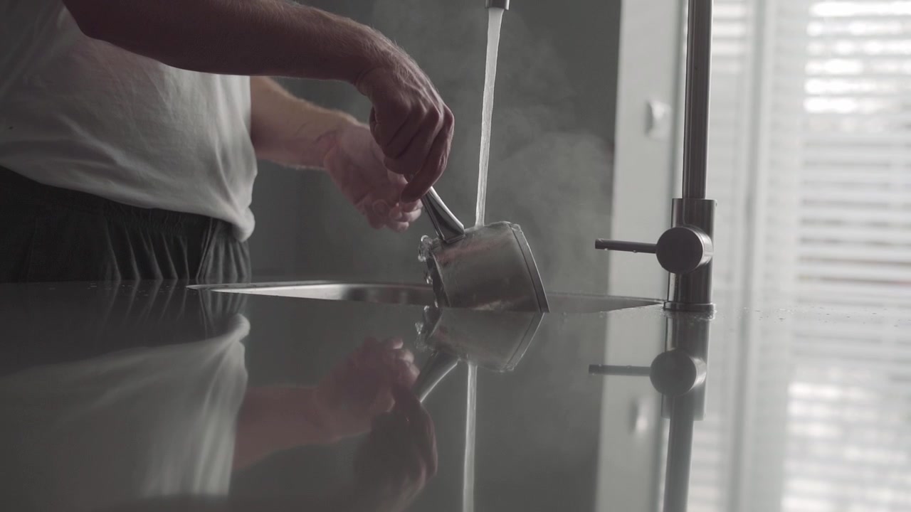 Cleaning dishes pots and pans with hot water and mist in a minimalist modern kitchen