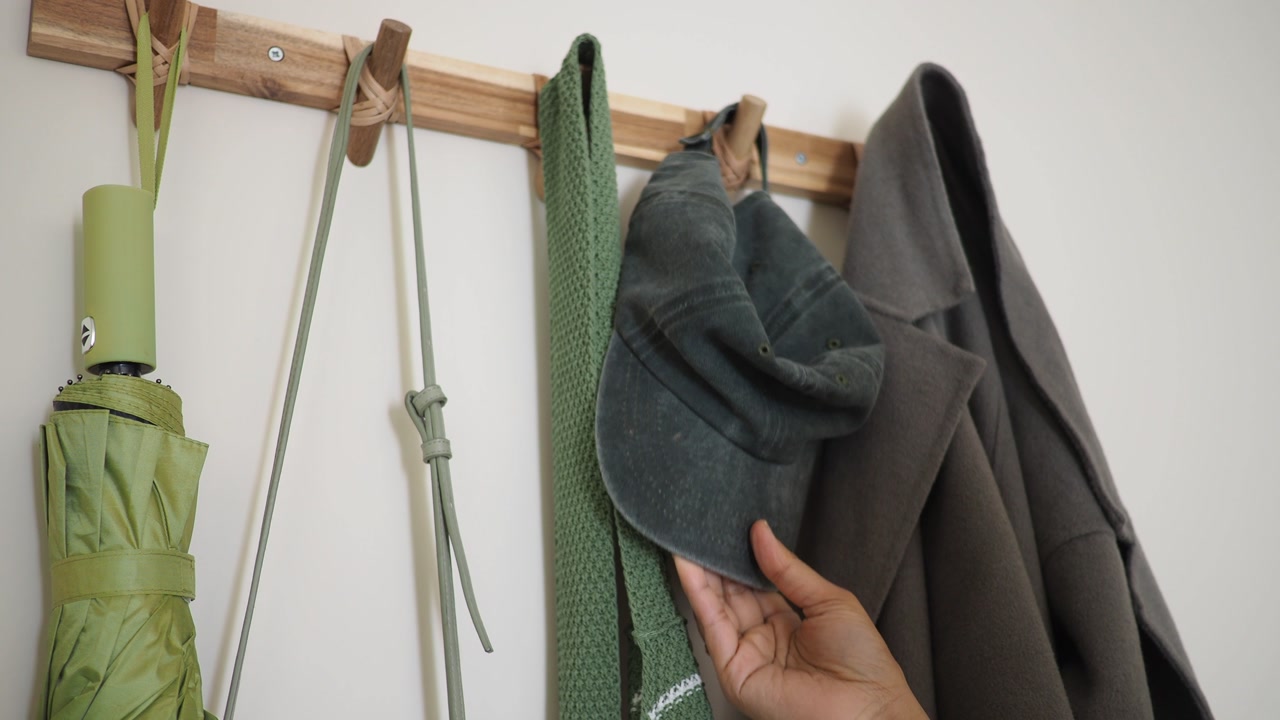 Hand Taking Green Baseball Cap from Wooden Coat Rack