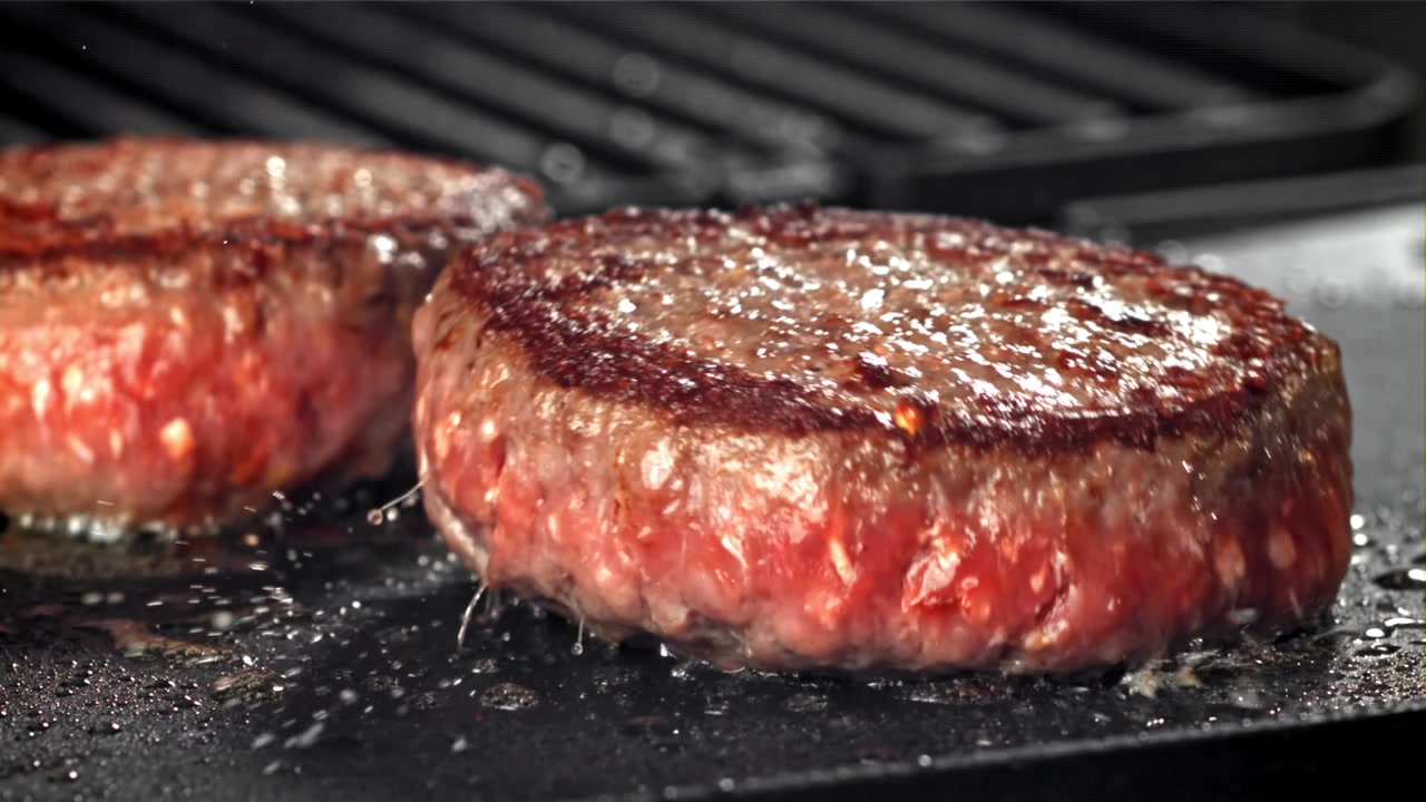 Hamburger di manzo fresco che sfrigola su una piastra calda