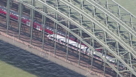 Aerial-view-of-trains-crossing-a-bridge-over-a-river,-with-clear-skies-and-a-dynamic-perspective