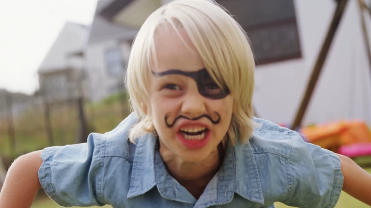 뒷마당에서 점프하는 얼굴 페인트를 가진 행복한 소년 4k