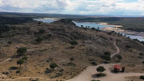 Vuelo-Con-Dron-Sobre-Un-Oppidum-Celta-De-La-Edad-De-Hierro-Visualizando-Parte-De-Sus-Murallas-Reconstruidas-Y-La-Entrada-Al-Pueblo-Situado-Sobre-Una-Colina-De-Granito-Con-Un-Embalse-Al-Fondo-ávila,-España