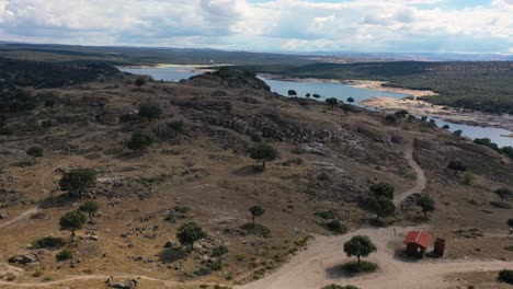 vuelo de avión no tripulado sobre un oppidum celta de la edad del hierro visualizando parte de sus murallas reconstruidas y la entrada a la ciudad ubicada en una colina de granito con un embalse en el fondo ávila, españa