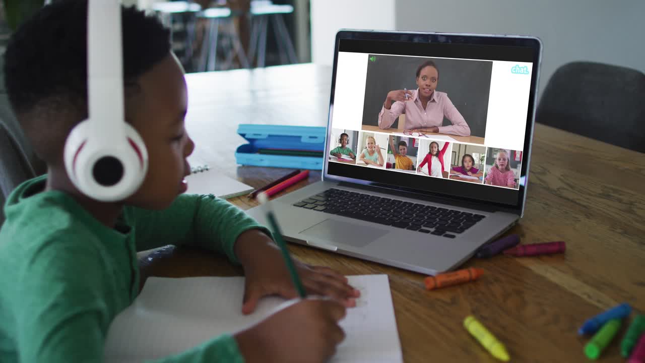 Schoolboy using laptop for online lesson at home, with diverse teacher and class on screen
