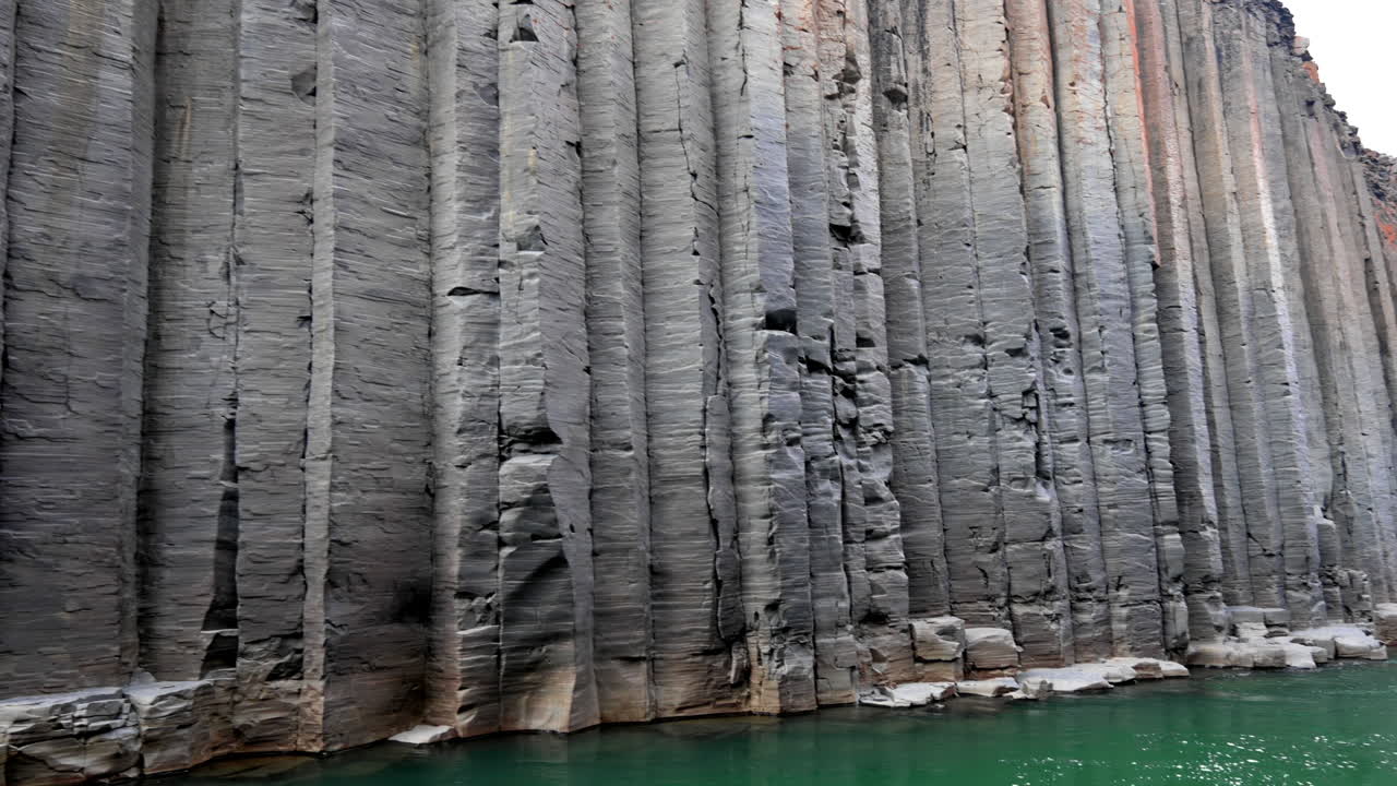 altas columnas de basalto gris con puntos de naranja en un cañón con río verde
