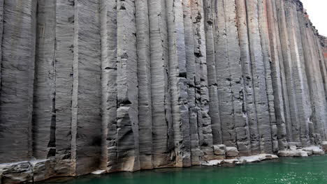 high grey basalt columns with dots of orange in a canyon with green river