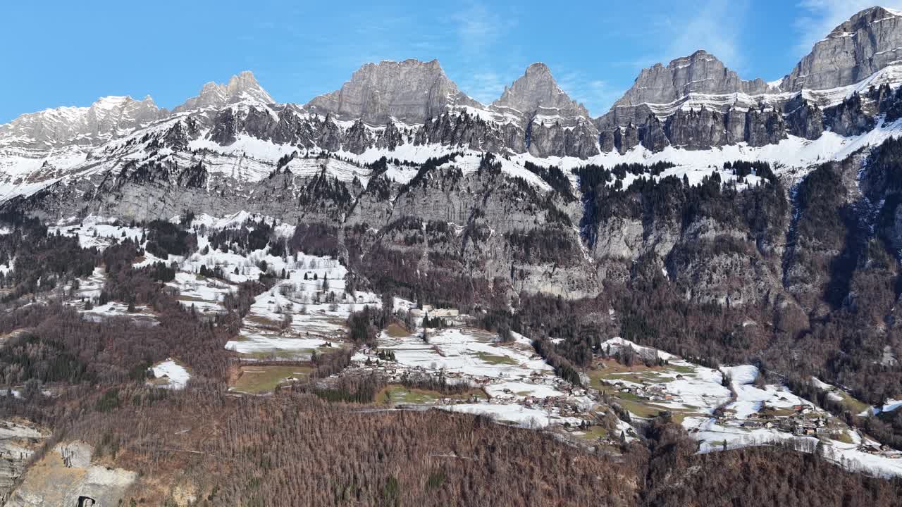 Aerial of the snow-dusted Churfirsten mountain range in Switzerland. Towering limestone cliffs overlook the winter valley and the deep blue waters of Lake Walensee