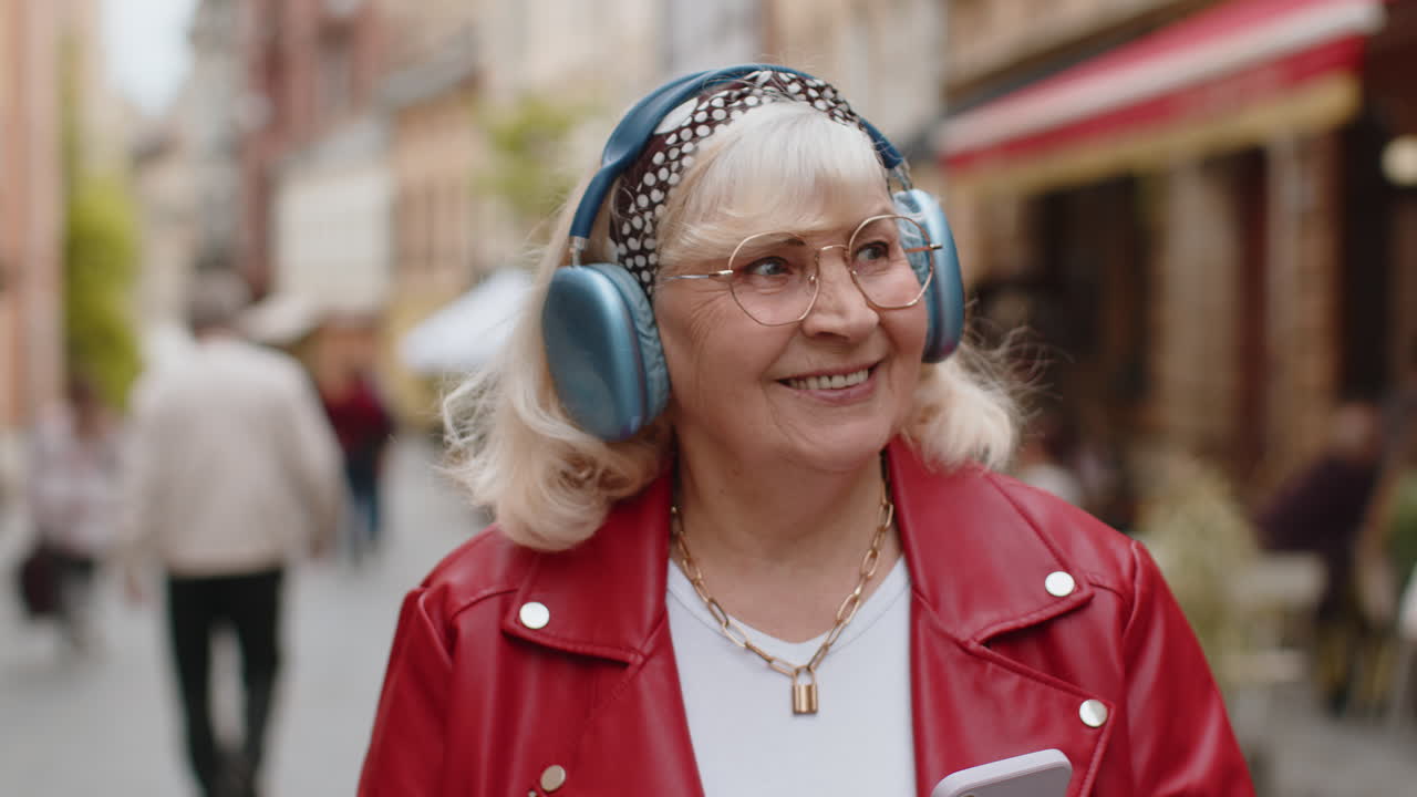 Una donna anziana felice con le cuffie wireless sceglie di ascoltare musica con lo smartphone ballando all'aperto