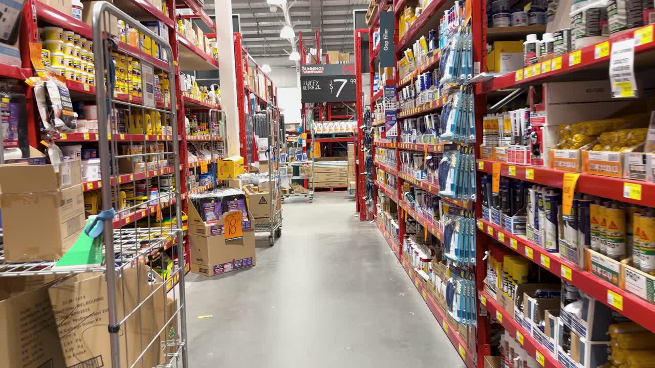 Camera moves through hardware store aisle with paint, glue, and tools under bright lighting