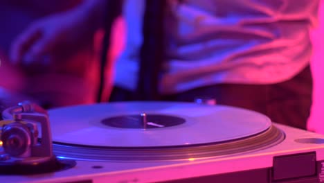 vinyl scratched on turntable during live performance with warm pink and blue lighting setup, filmed as close up on hand motion