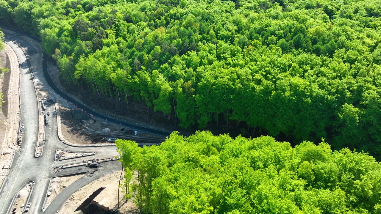 Cinematic aerial shot of a new road being built through a dense green forest in Gdynia. Showcases infrastructure development and sustainability in urban planning.