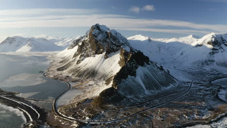 Drone-shot-around-a-snowy-landscape-with-rocky-peaks,-golden-hour-in-Iceland