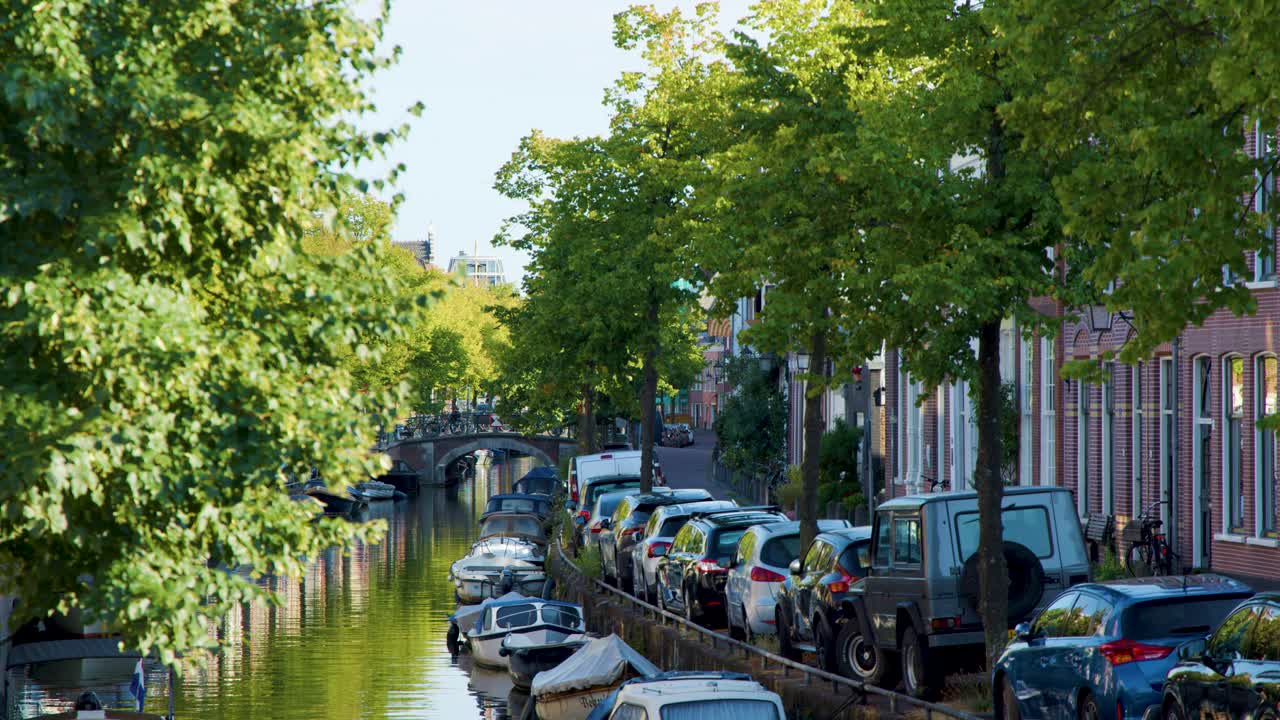 Sunny canal lined with boats, cars, trees, and historic buildings in Haarlem, Netherlands