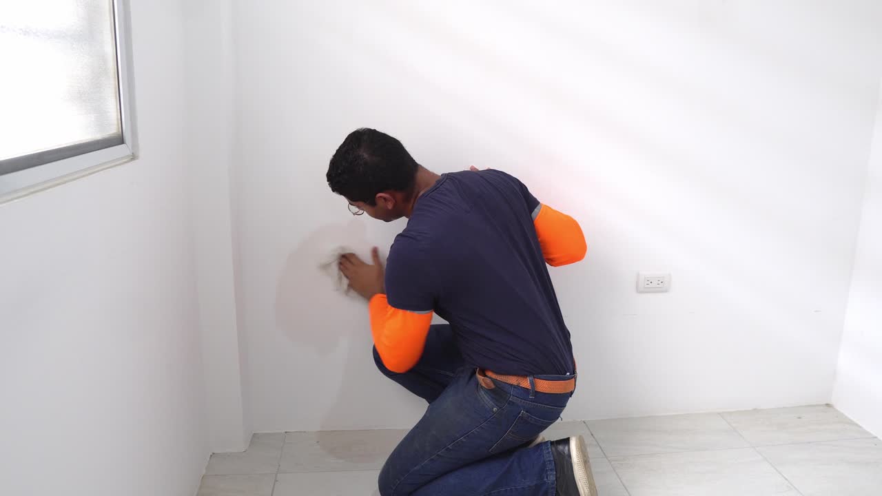 hombre en el trabajo limpiando la pared interior de la habitación recién pintada en la casa