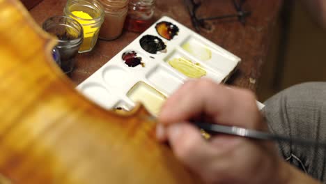 focused luthier varnishing violin in workshop