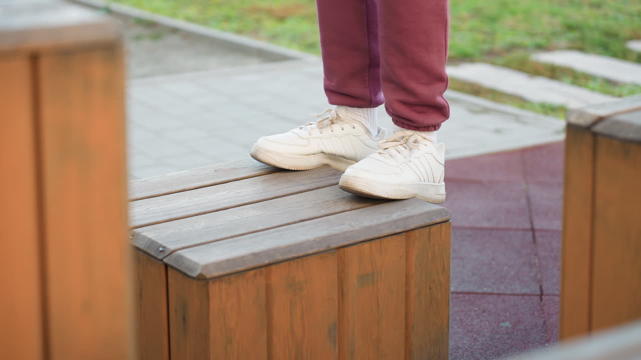 Side view legs of female athlete in white trainers exercising on wooden jump box outdoors on gym floor demonstrating balance control strength and power during intense workout