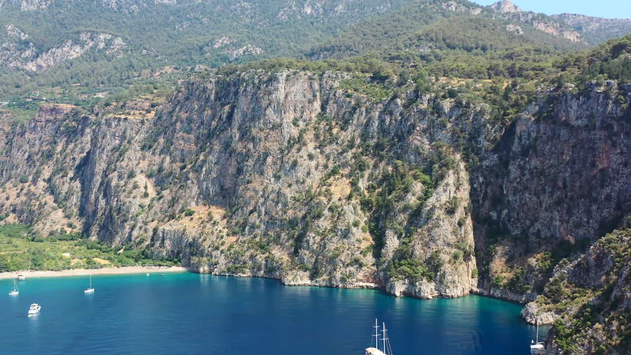 aerial drone panning up towards the large green mountains of Butterfly Valley while boats are anchored in the blue ocean of Fethiye Turkey