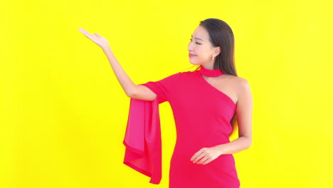 an attractive young woman in a red off the shoulder dress gestures with her hand palm up to one side of the frame