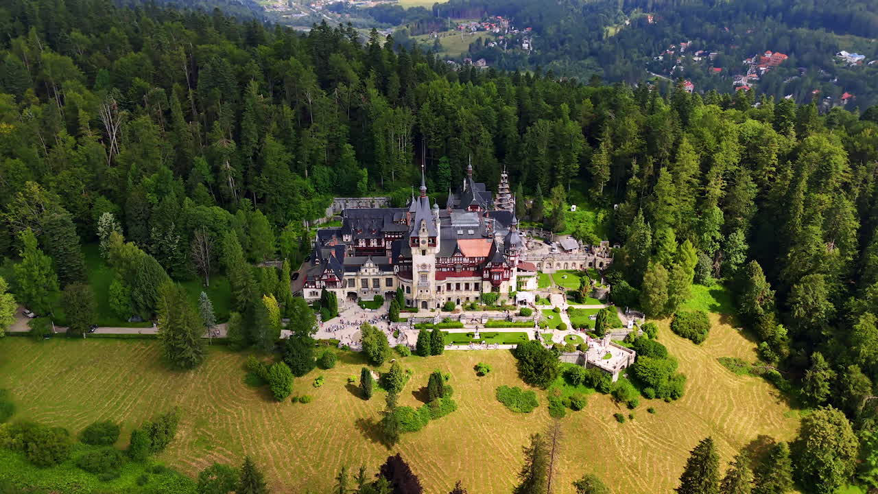 Pine tree wood and meadow surround the Peles Castle in Sinaia, the Carpathians, Romania. Drone flight over the building on sunny day