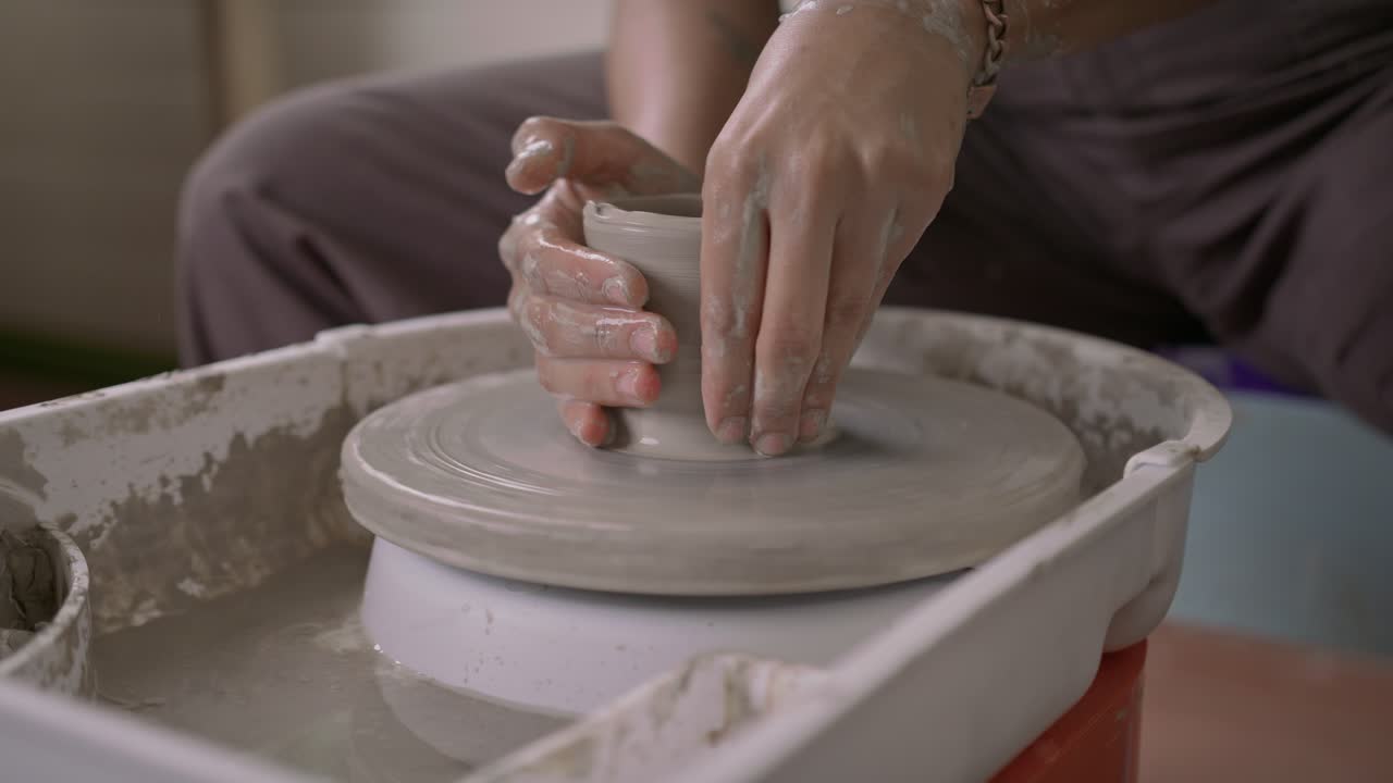 el trabajador de la cerámica agrega agua a la olla de arcilla para formar hábilmente la forma con manos hábiles en cámara lenta