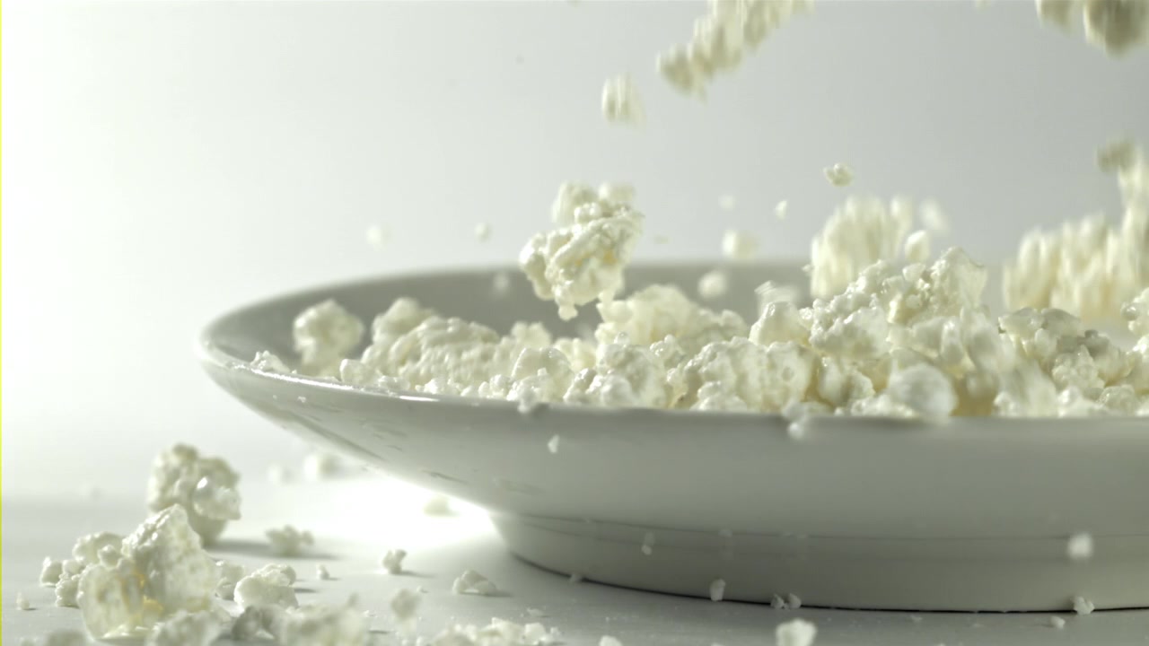 Hytteost falder ned i en hvid tallerken i slowmotion