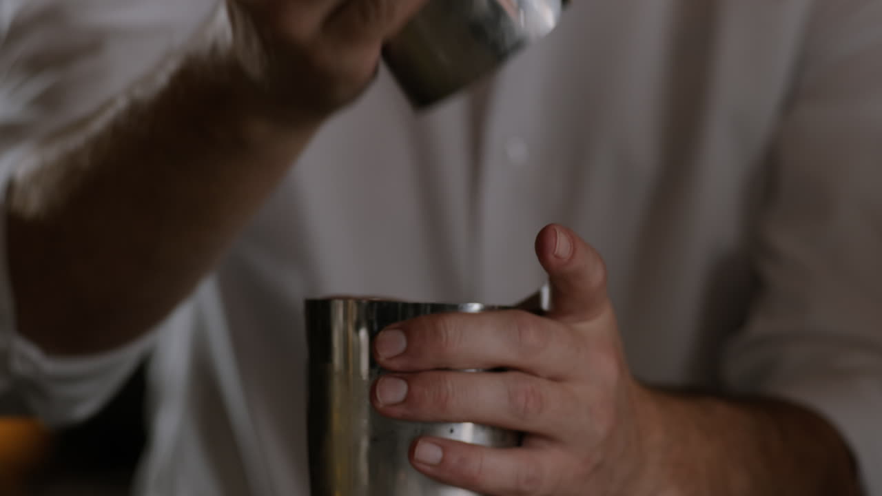 Un barman apre uno shaker per cocktail e si prepara a versarlo in un bicchiere pieno di ghiaccio