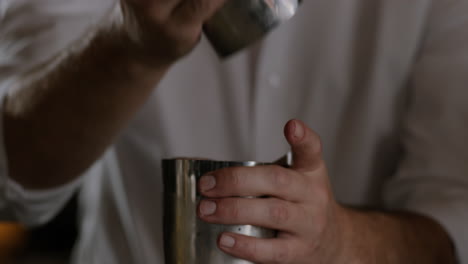 bartender opens up a cocktail shaker and prepares to pour it into a glass full of ice