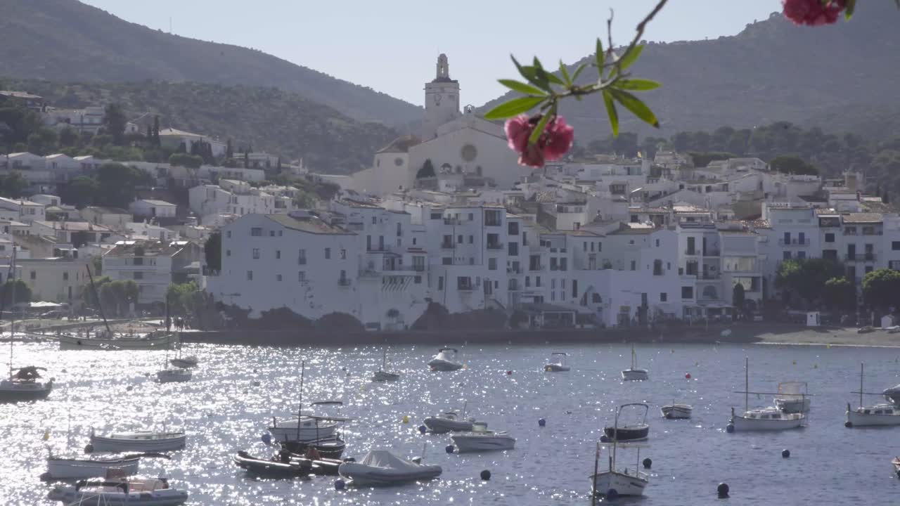 Beautiful church in coast town, Costa Brava, Spain, boats in the ocean, flower in the foreground, static shot