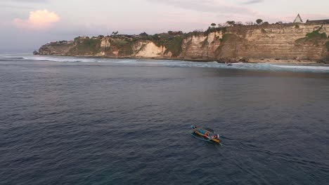 tourists in the traditional balinese boat cadik approaching the fortified cliffs with hidden temple, pura luhur, uluwatu, bali, indonesia