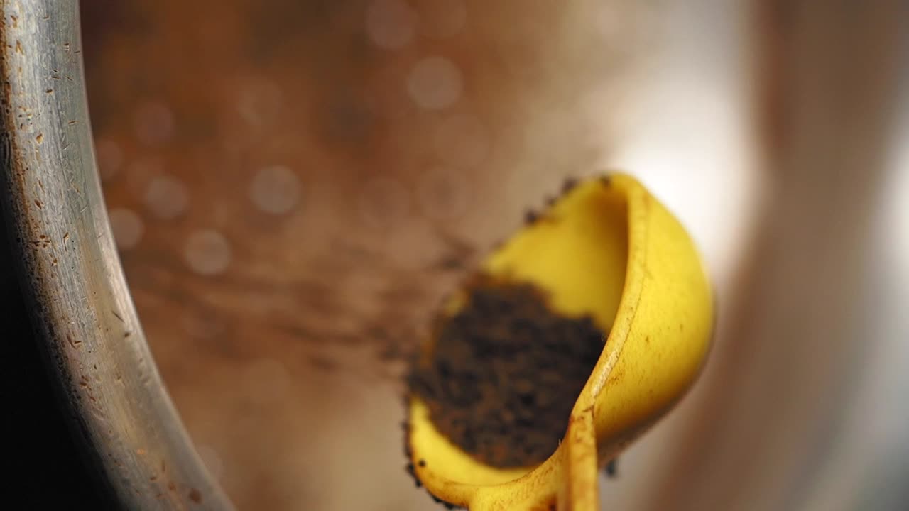 A close-up of a yellow measuring spoon filled with dark coffee grounds or tea leaves, some spilling out