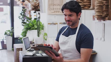 retrato del propietario masculino de una floristería trabajando en una tableta digital detrás del mostrador de ventas - filmado en cámara lenta