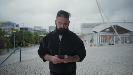 Cheerful-young-bearded-man-using-smartphone.