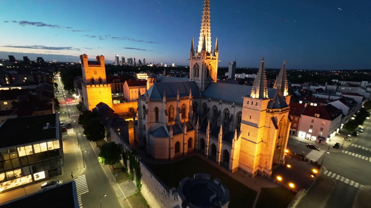 Starting drone approaching cathedral over city center at twilight, revealing lit spire and tower