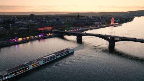 sunset drone flight of mainz over the rhine river crossing a boat and the main city bridge in front of orange sky