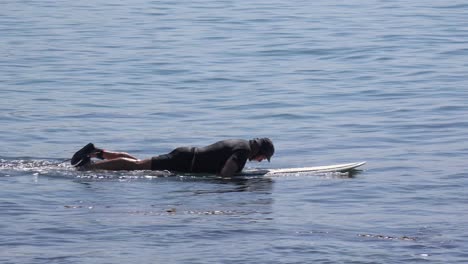 a middle aged surfer dude paddles his board in the waves on a southern california beach