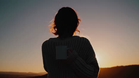 Silhouetted Person Holding a Mug Against a Sunset