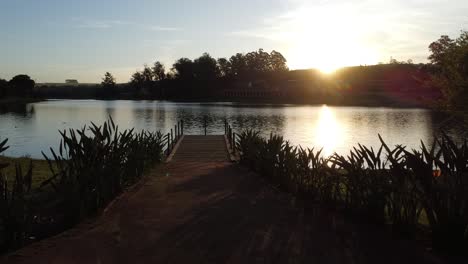 Vorwärtsbewegung-Mit-Drohne-Bei-Wunderschönem-Sonnenuntergang-Am-See-Mit-Pier-Und-üppiger-Natur