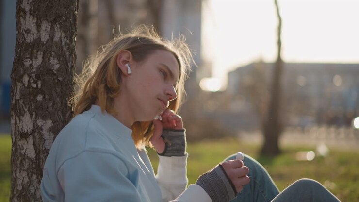 teen unwinding with outdoor tunes, juvenile individuals soaking in melodies beneath clear city sky, adolescents leisurely experiencing rhythmic sounds outdoors on sunny metropolitan afternoon