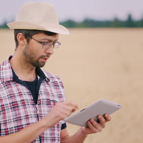 Farmer-uses-a-tablet-stands-against-the-background-of-a-wheat-field