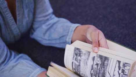 asian female student wearing a blue hijab lying on the floor and reading a book