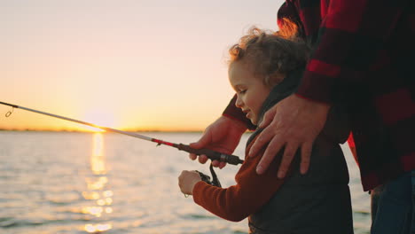 joyful little boy is enjoying joint family fishing with father or grandpa in river shore smiling child