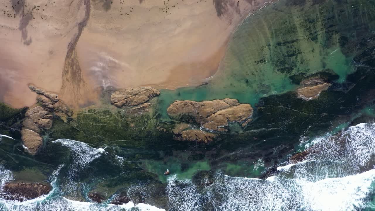 Scenic aerial view of California coast and the Pacific Ocean waves crashing against rocky terrain and beach.