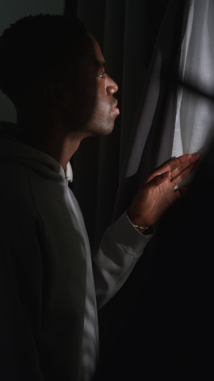 video vertical de un joven infeliz y deprimido en casa mirando por la ventana sufriendo de agorafobia o paranoia 2