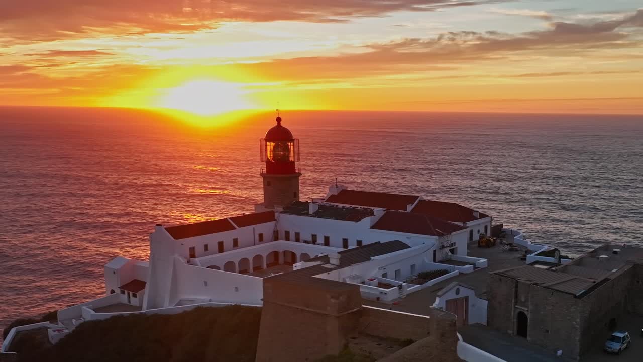 Una splendida ripresa aerea al tramonto del faro con vivaci tonalità arancioni e rosa nel cielo.