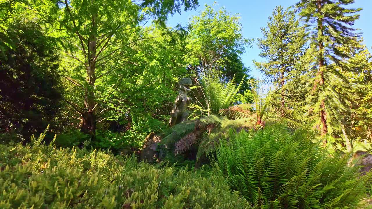 Lateral view of prehistoric garden showing ferns, trees, and a T-Rex statue at Haute Bretagne Botanical Park - France