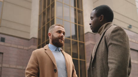 Bottom-view-of-caucasian-and-african-american-businessman-in-elegant-clothes-talking-in-the-street-in-autumn