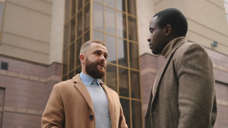 vista inferior del hombre de negocios caucásico y afroamericano con ropa elegante hablando en la calle en otoño