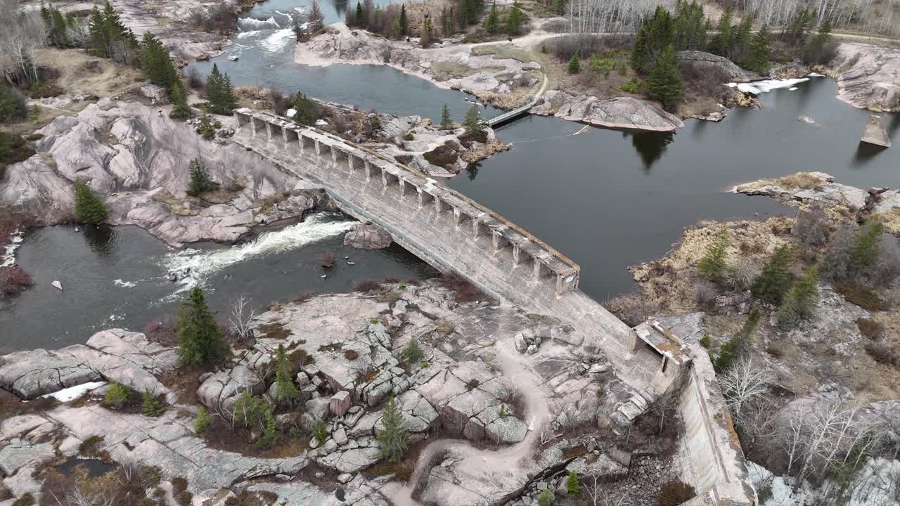 İlkbaharda Manitoba Miras Parkı'ndaki tarihi Pinawa Barajı'nın drone ile havadan çekilmiş görüntüsü. Yerde kar kalıntıları, çevredeki boreal ormanı, nehir ve eski hidroelektrik kalıntıları görünüyor.